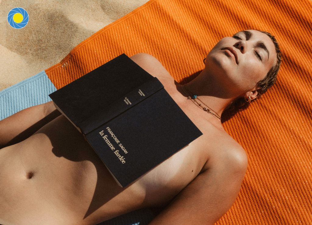 Une femme nue allongée sur le sable d'une plage des Landes avec un livre de Françoise Sagan sur sa poitrine